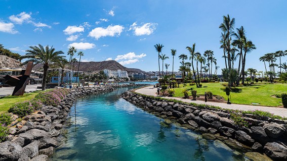 Ruhige Badebucht mit klarem Wasser, heller Sandstrand und terrassenförmig gebaute Hotelanlagen am Hang.